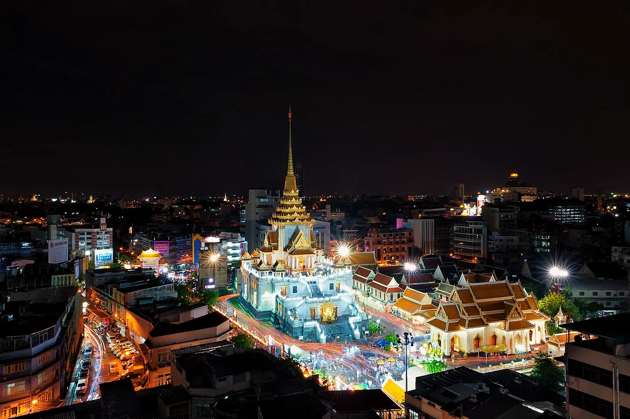 เห็นทั้งตัววัดไตรมิตรวิทยารามวรวิหารจากมุมสูง โดยเห็นตัววัดสีขาวและหลังคาวัดสีเหลืองทองอร่าม พร้มอกับแสงไฟที่ประดับอยู่รอบวัดและลานหน้าวัด